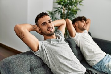 Two hispanic men couple smiling confident relaxed with hands on head at home