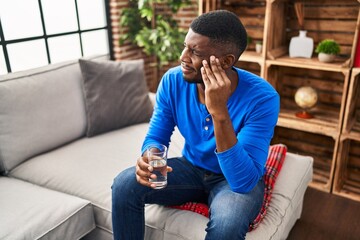 Poster - Young african american man with headache holding glass of water at home