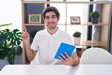 Canvas Print - Young hispanic man using touchpad sitting on the table smiling happy pointing with hand and finger to the side