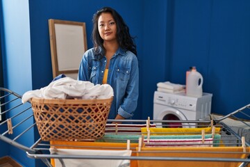 Poster - Young asian woman hanging clothes at clothesline relaxed with serious expression on face. simple and natural looking at the camera.