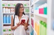 © Krakenimages.com - Young beautiful hispanic woman customer smiling confident using smartphone at pharmacy