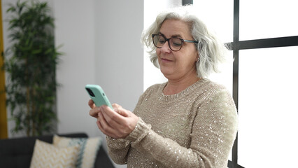 Canvas Print - Middle age woman with grey hair using smartphone standing at home