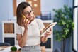 © Krakenimages.com - Young beautiful hispanic woman business worker talking on smartphone reading notebook at office