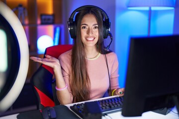 Canvas Print - Young hispanic woman playing video games smiling cheerful presenting and pointing with palm of hand looking at the camera.