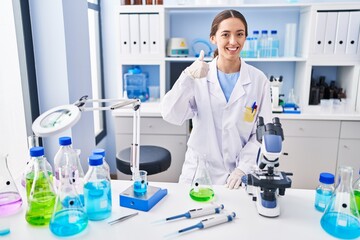 Poster - Young brunette woman working at scientist laboratory smiling happy and positive, thumb up doing excellent and approval sign