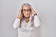 © Krakenimages.com - Middle age woman with grey hair standing over white background with hand on head, headache because stress. suffering migraine.