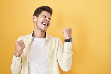 Wall Mural - Young hispanic man standing over yellow background celebrating surprised and amazed for success with arms raised and eyes closed. winner concept.