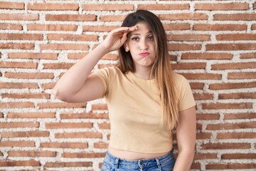 Sticker - Young brunette woman standing over bricks wall worried and stressed about a problem with hand on forehead, nervous and anxious for crisis