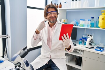 Poster - Handsome middle age man working at scientist laboratory doing video call smiling happy pointing with hand and finger