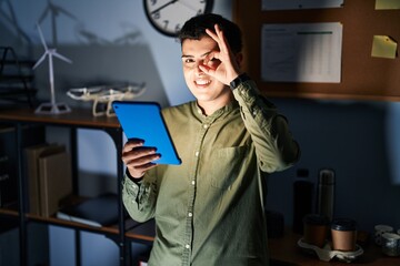 Canvas Print - Non binary person using touchpad device at night doing ok gesture with hand smiling, eye looking through fingers with happy face.