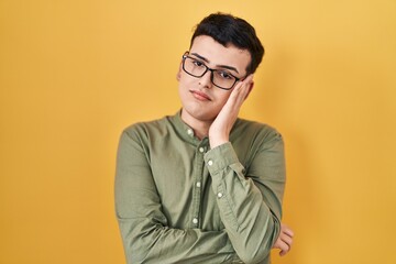 Sticker - Non binary person standing over yellow background thinking looking tired and bored with depression problems with crossed arms.