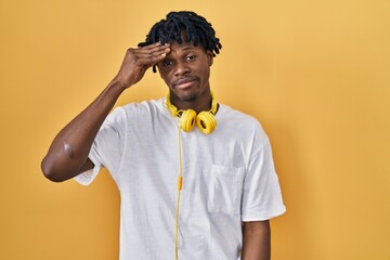 Young african man with dreadlocks standing over yellow background worried and stressed about a problem with hand on forehead, nervous and anxious for crisis