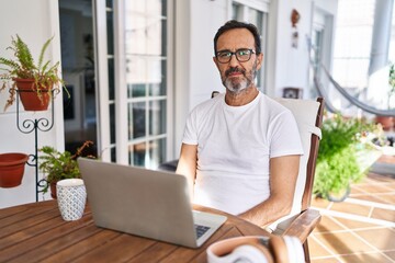 Wall Mural - Middle age man using computer laptop at home relaxed with serious expression on face. simple and natural looking at the camera.