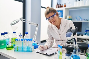 Sticker - Young blonde woman wearing scientist uniform writing on clipboard at laboratory