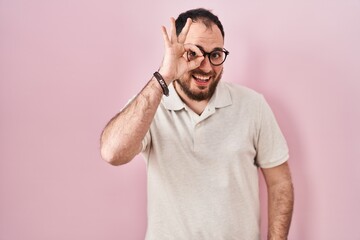 Canvas Print - Plus size hispanic man with beard standing over pink background doing ok gesture with hand smiling, eye looking through fingers with happy face.