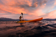 A Woman Is Paddling A Kayak At Sunset On Lake Tahoe.