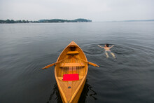 A Young Man Swims Next To A Small Antique Wooden Row Boat In The St. Lawrence River In Upstate New York's 1000 Islands.