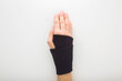 Young adult woman hand with protective black elastic wrist bandage on white table background. Closeup. Top down view.