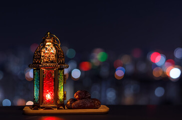 Wall Mural - Lantern and small plate of dates fruit with night sky and city bokeh light background for the Muslim feast of the holy month of Ramadan Kareem.