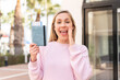 © luismolinero - Young blonde woman holding a passport at outdoors shouting with mouth wide open