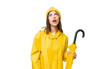 Wall Mural - Young Russian woman with rainproof coat and umbrella over isolated chroma key background looking up and with surprised expression