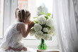 © alexkich - A little girl is sitting on the windowsill. A bouquet of flowers in a vase by the window and a girl sniffing flowers. A little princess in a white dress with a bouquet of white flowers by the window.