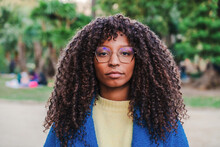 Close Up Portrait Of Young Serious African American Woman With Goggles And Curly Hair Looking Pensive At Camera With Sad Attitude. Front View Of Multiracial Girl Standing At Park Outdoors. High