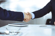 © rogerphoto - Business people shaking hands while sitting at the desk at meeting or negotiation, close-up. Group of unknown businessmen in a modern office. Teamwork, partnership and handshake concept