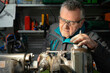 © Irina - A man in safety glasses and a work uniform sets up a grinding machine in his workshop. The grinding machine details in focus. In the background are various working tools on the metal shelving for