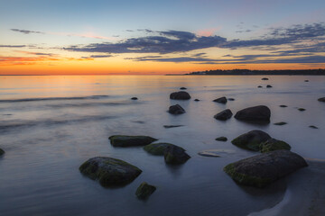 Wall Mural - Red colored sky over a rocky seashore. Sunset landscape.