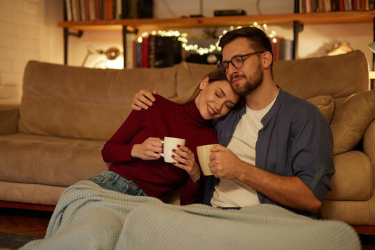 young couple drinking tea while sitting in the living room at night.