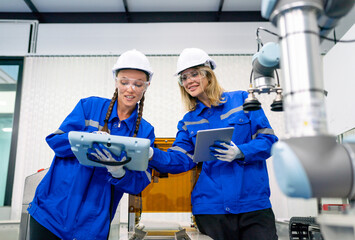 Two pretty professional technician or engineer women help to check the system use controller and ipad with robotic machine in factory workplace.