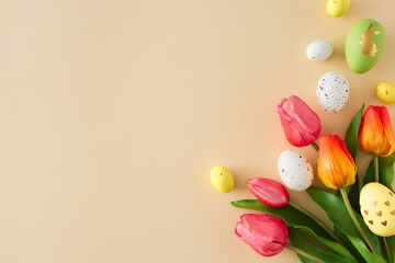 Wall Mural - Easter decor concept. Flat lay photo of colorful eggs and tulips flowers on isolated beige background with copy space. Holiday card idea