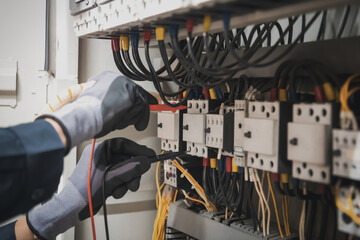 Electricity and electrical maintenance service, Engineer hand holding AC multimeter checking electric current voltage at circuit breaker terminal and cable wiring main power distribution board.