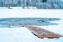 An Ice Hole On A Frozen Lake With A Snow-covered Wooden Path Descending Into The Water