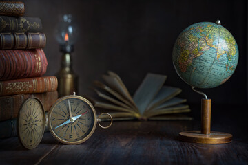 Wall Mural - Old earth globe, compass, books and lamp on the table. In the cabinet of a traveler, explorer, discoverer. Concept on the theme of travel, world exploration, antiquity, history, geography. 