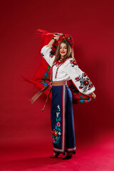 Wall Mural - Portrait of ukrainian woman in traditional ethnic clothing and floral red wreath on viva magenta studio background twirls a handkerchief. Ukrainian national embroidered dress call vyshyvanka