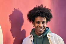 Close Up Portrait Photo Of Young Stylish Happy African American Cool Hipster Guy Face Laughing On Red City Wall Lit With Sunlight. Smiling Cheerful Cool Gen Z Male Model Standing Outdoors. Headshot.