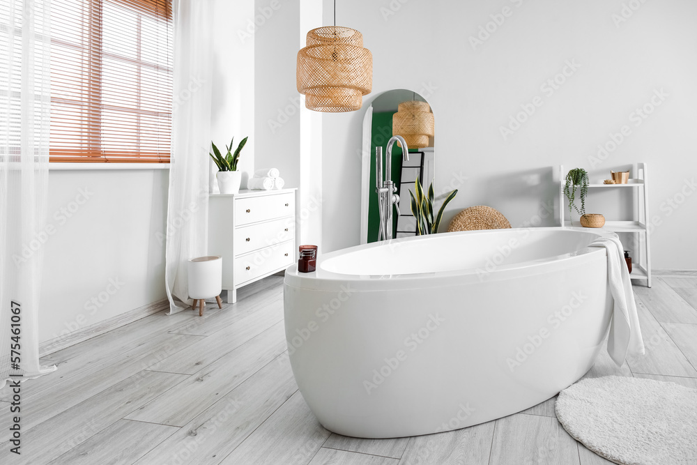 Interior of light bathroom with bathtub, drawers and mirror