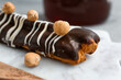 Board with delicious chocolate eclair and hazelnuts on grey table