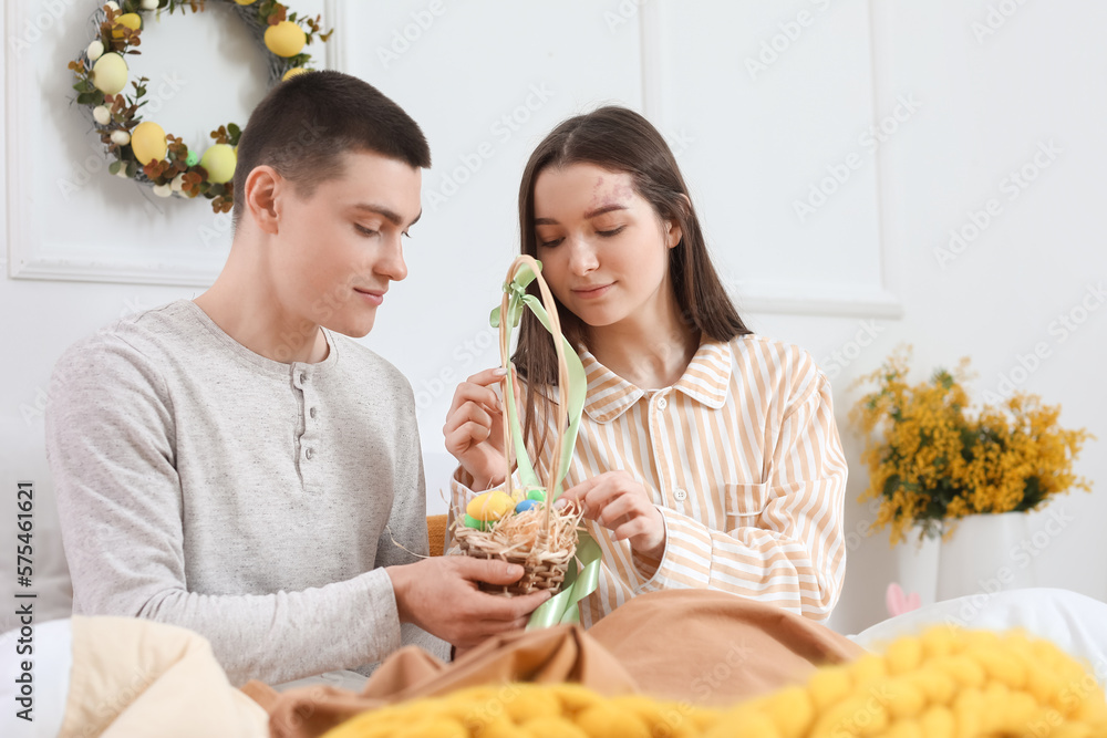 Happy young couple with basket of Easter eggs in bedroom