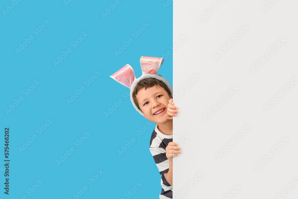Cute little boy with Easter bunny ears and blank poster on blue background