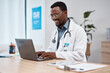 © Anela R/peopleimages.com - Black man, doctor and laptop with smile in healthcare for research, medicine or PHD at clinic desk. Happy African American male medical professional smiling, working or typing on computer at hospital