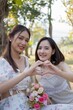 © Natee Meepian - Asian woman friends, they are having picnic,they talk happily,charming Asian woman makes a heart hand sign with her friend while picnic in the park