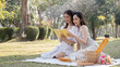 © Natee Meepian - Two young Asian women beautiful read a book while picnicking in the beautiful garden together on the weekend