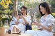 © Natee Meepian - Asian women sit on picnic chairs, focusing on using their smartphones asian woman friends, they are having picnic,they talk happily