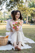 © Natee Meepian - Charming beautiful young Asian woman in a lovely dress, holding a flower bouquet, enjoying a picnic with her friend in the park