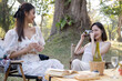 © Natee Meepian - Charming Asian woman enjoying picnic in the park with her friend, taking photo with camera, having special moment on the weekend together