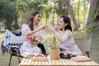© Natee Meepian - Asian woman friends, they are having picnic,they talk happily,charming Asian woman makes a heart hand sign with her friend while picnic in the park