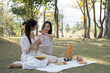 © Natee Meepian - Two charming Asian women in beautiful dresses sitting on picnic cloth, having an tea picnic party together in the garden